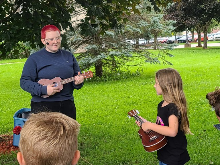 ukulele instructor demonstrates to young girl