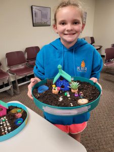 girl in blue sweatshirt with fairy garden in round container