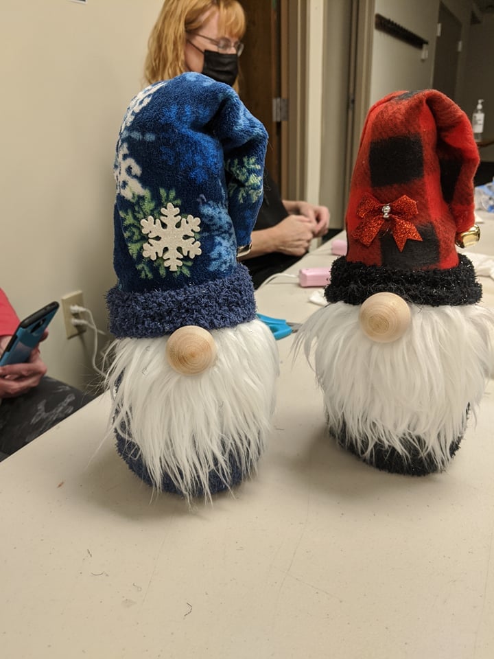 one gnome with dark blue hat with snowflake pattern, one gnome with red and black plaid hat with glitter bow on front