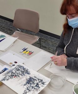 red haired woman works on watercolor painting