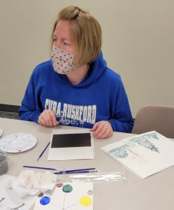 blonde haired woman works on watercolor paintings