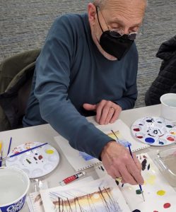 man works on watercolor of trees at sunset