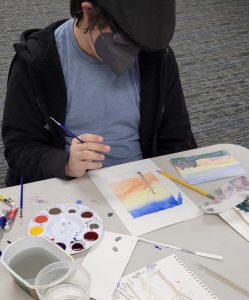 teen boy works on watercolor painting of tree at sunset