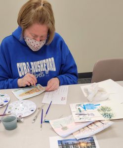 blonde haired woman works on autumn landscape watercolor