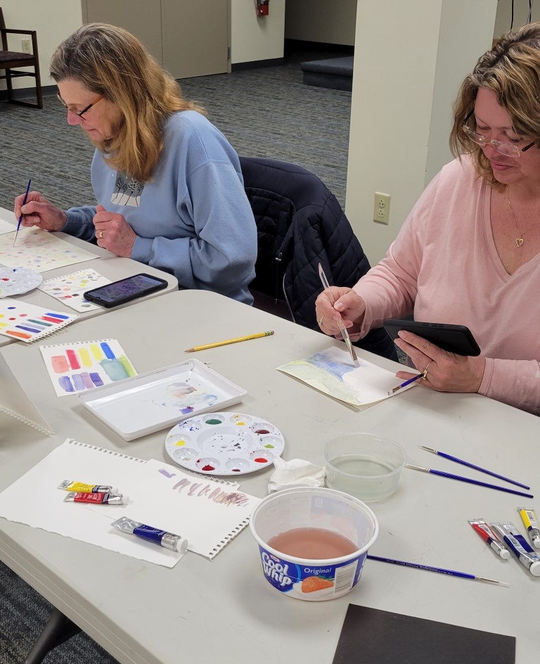 two women work on watercolor paintings