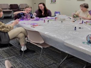 Woman watches her daughter add ink to large glass vase while two other women work on their projects