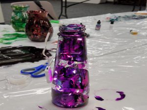 Foreground: Pink, purple and blue ink on narrow glass jar with LED light string; background: vase with red ink and vase with green and gold ink