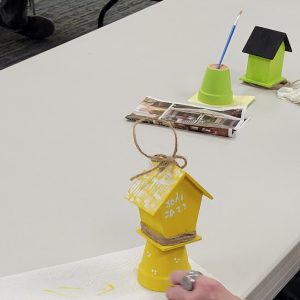 yellow mini birdhouse with white decorative details perched on yellow pot & bright green birdhouse with black roof