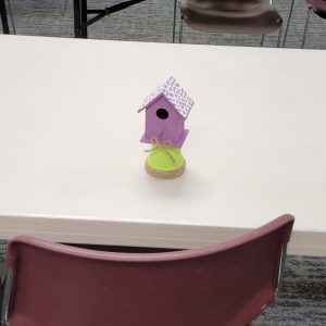 light purple mini birdhouse with white shingles perched on light green flower pot with twine wrapping the base