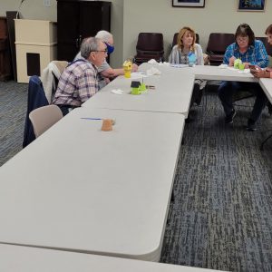 five people sit at tables with colorful mini birdhouse crafts in front of them