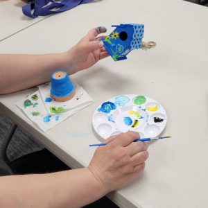 person shows the yellow and light blue flowers on the front of their dark blue mini birdhouse