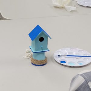 light blue mini birdhouse with blue roof perched on a miniature light blue pot with blue stripe and twine decoration