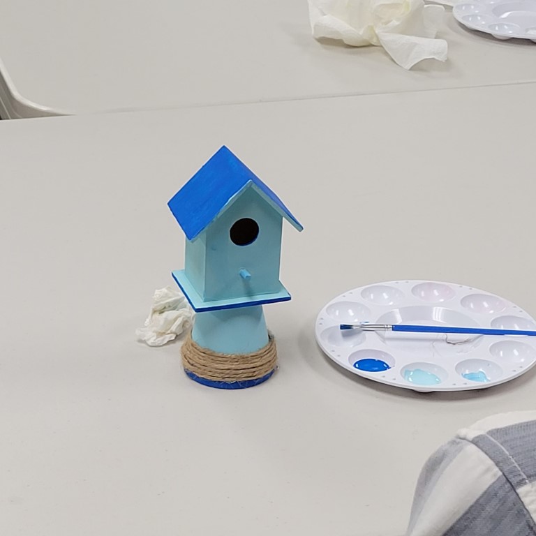 light blue mini birdhouse with blue roof perched on a miniature light blue pot with blue stripe and twine decoration