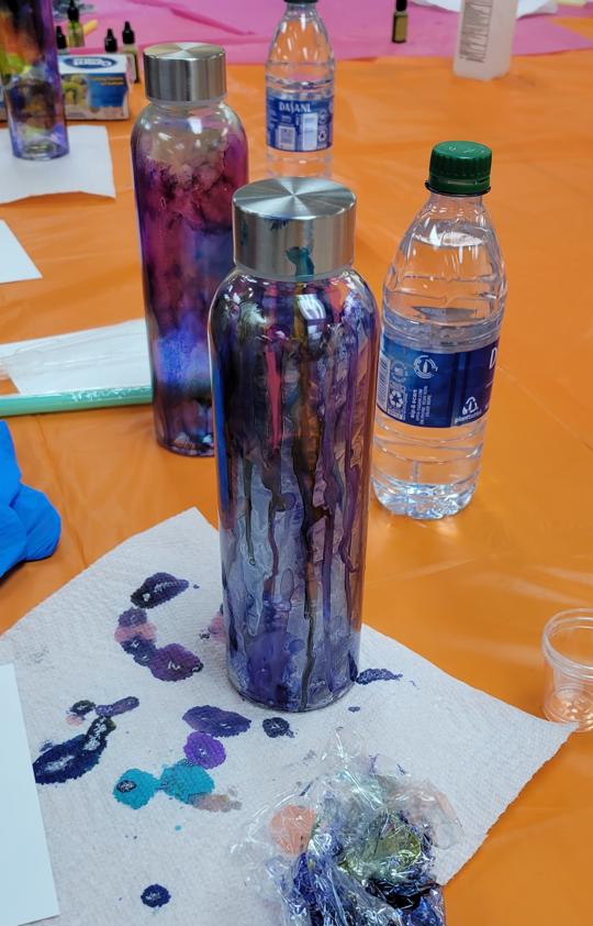 bottle with blue, purple, pink, silver ink in foreground with purple, red, and blue bottle in background