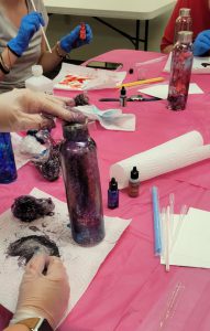 bottle with purple, red, and silver in foreground with other ink projects in background