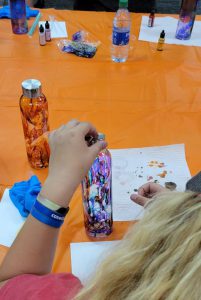 blond girl holds a bottle with drips of purple, blue, and red