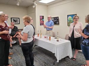 several people converse near a table with bottles of wine