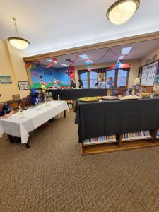 bookshelves draped in black tablecloths display hors d'oeuvres near a table with a white cloth displaying wine