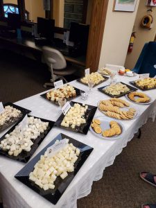 table with white lace cover and several black trays with cubes of cheese and round platters of crackers