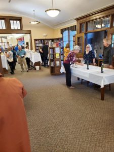 several people visit tables of hors d'oeuvres and wine in a library