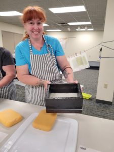 red haired woman holds wooden framed screen box for making handmade paper