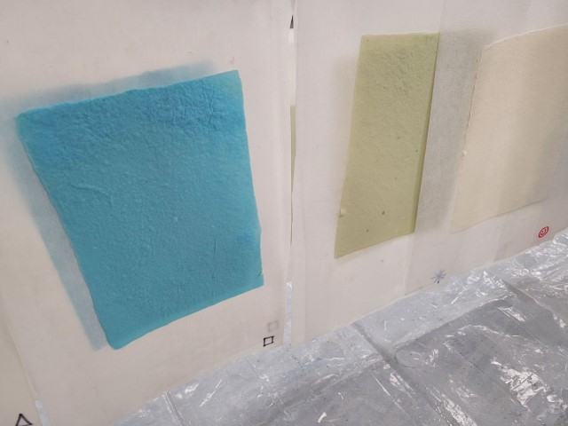 handmade paper in shades of blue, green, and cream hang to dry
