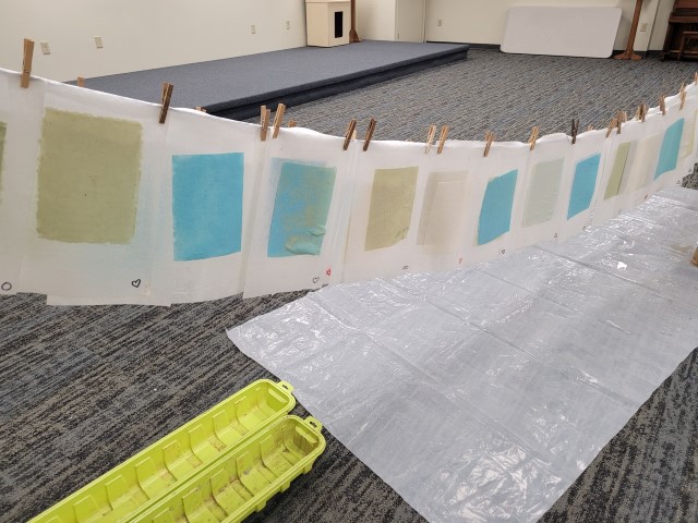 several sheets of handmade paper in various shades hang on a line to dry