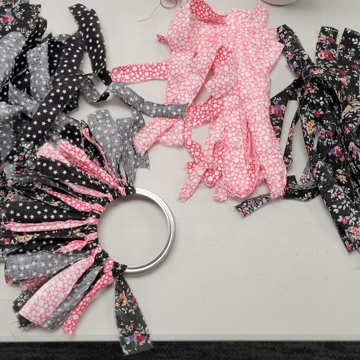 fabric strips in black floral, magenta with white dots, and black with white stars sits on a table with a mason jar lid that has fabric strips tied halfway around the perimeter
