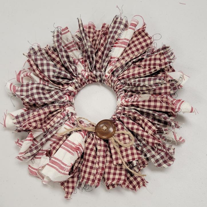 wreath made with strips of fabric in maroon gingham, maroon and black plaid, and cream and maroon stripe
