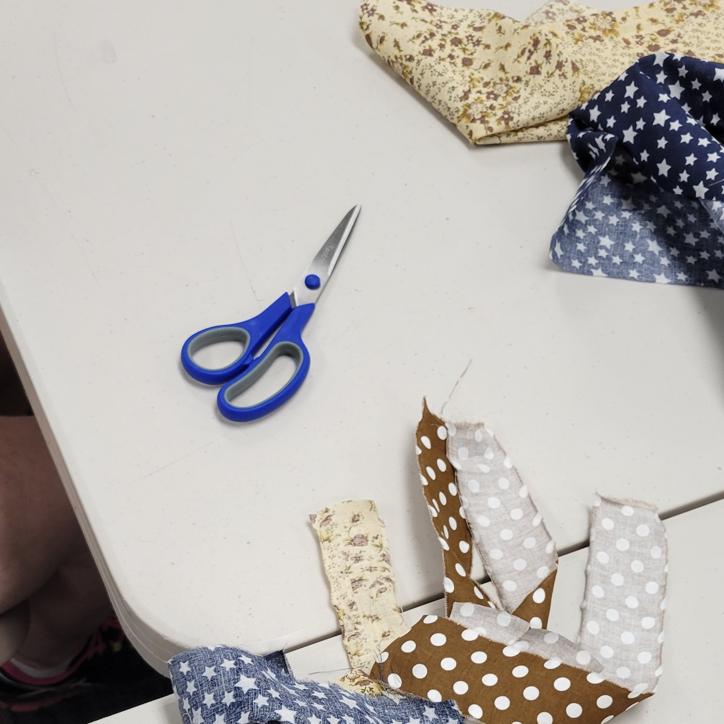strips of fabric in navy with white stars, cream with mauve flowers, and brown with white dots sit on a table with a pair of blue handled scissors