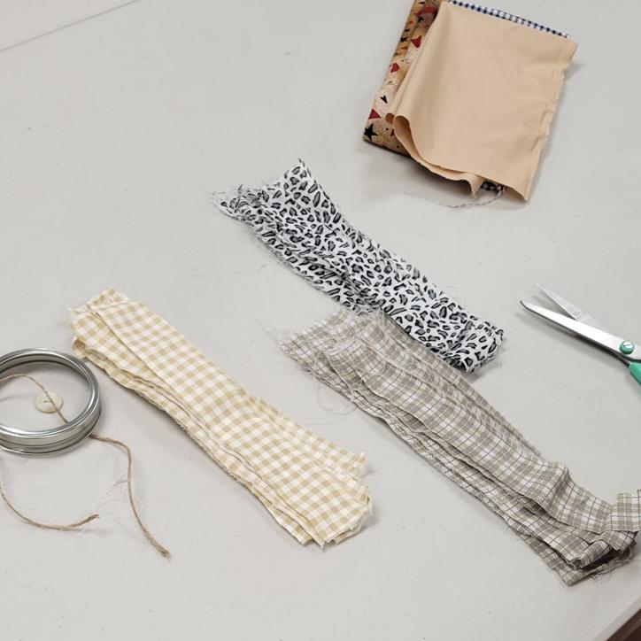 strips of fabric in tan gingham, khaki plaid, and white with grey leopard print sit on a table with a mason jar screw on lid