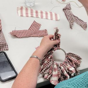 a pair of hands tying strips of fabric in maroon plaid and gingham to a mason jar screw on lid