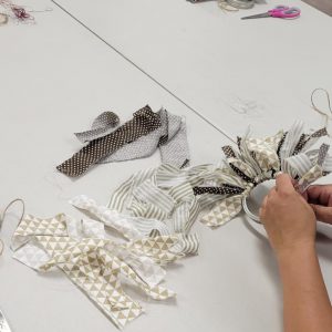 a pair of hands tying strips of fabric in shades of tan and brown to a mason jar screw on lid