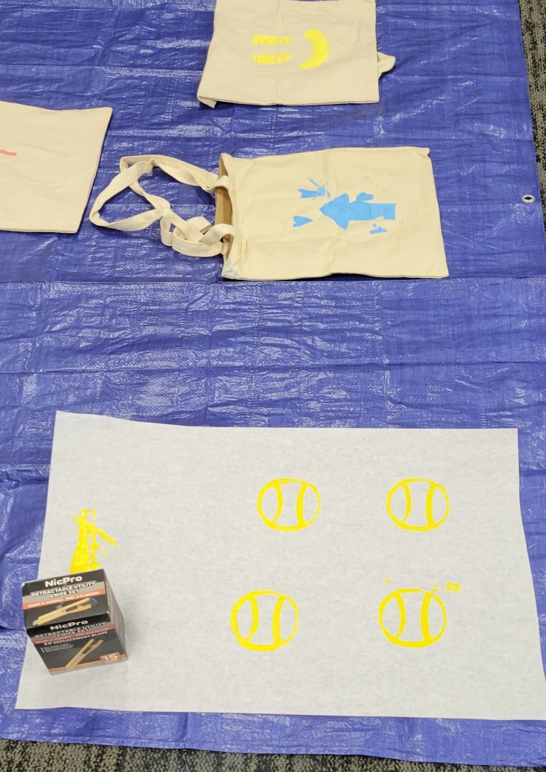 paper with four yellow baseballs, background has two tote bags with smiley and arrow pattern
