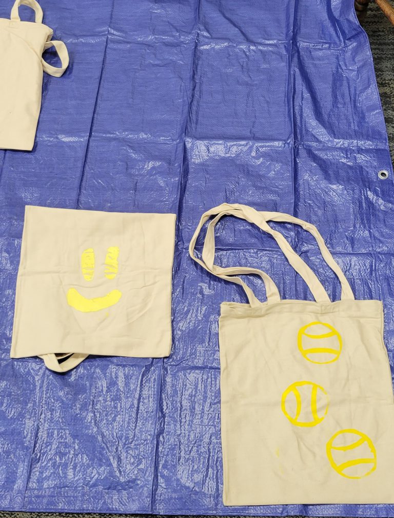two tan tote bags one with yellow smiley and one with yellow baseballs