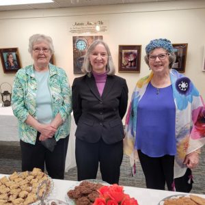 a trio of ladies smile for the camera with a table of cookies in front of them