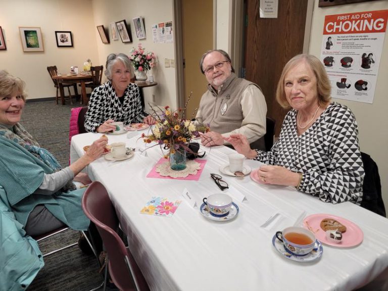 three women and one man smile for the camera as they enjoy tea and snacks