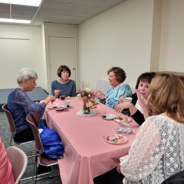 a table of ladies converse over tea and snacks