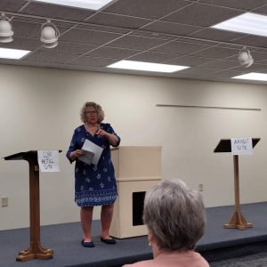 woman in a blue and white dress stands on a stage with a podium and two lecterns