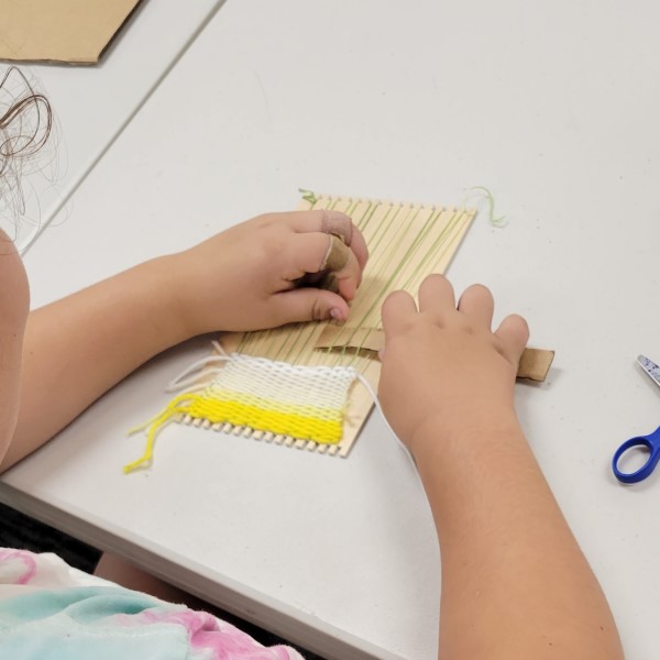 girl creates a small weaving project of yellow and white yarn
