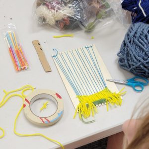 weaving project with yellow and green yarn and yellow tassels on a small weaving board