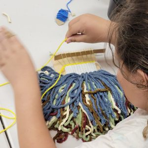 weaving project with multiple colors of yarn and a pile of fringe on a small weaving board