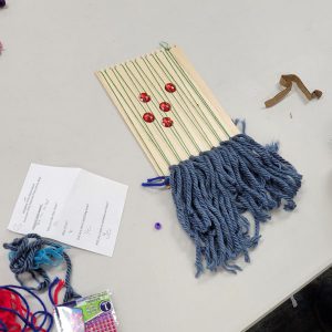 weaving project with blue fringe on a small weaving loom