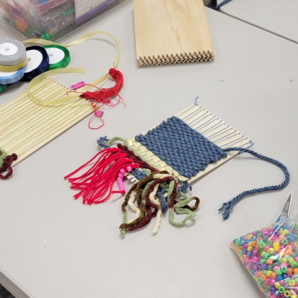 weaving project with several colors of yarn, ribbon, tassels and beads