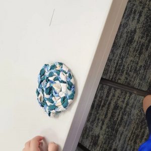 a circular rug of braided fabric in green blue and cream sits on a table