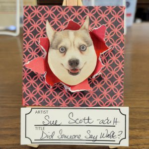 mixed media art with black background with red wedding ring quilt pattern and hole torn in center with red background showing through and dog face poking through