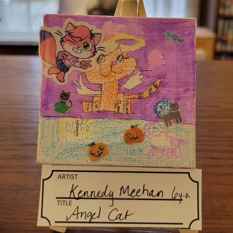 painting with pinky-purple background and blue base with orange cat with white wings and halo and pink cat wearing clothes sticker, small black and grey cat stickers, two jack-o-lantern stickers, and bat sticker