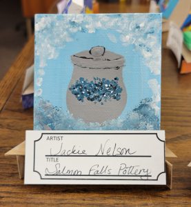 blue painting with frame of white, grey and blue dots around a grey pot with lid and blue flower design