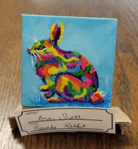 painting with blue background and rabbit in splotches of yellow, green, blues, pink, purples, red, and orange.