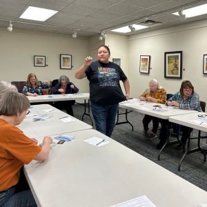 artist Samantha Jacobs instructs the group of women and girls in bracelet making